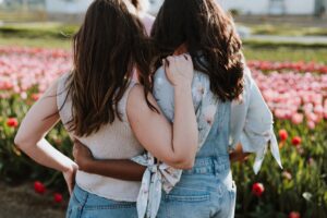 Two young women, one is brunette with pale skin and one is also brunette with dark skin. They have their arms wrapped around one another. Anti-racist friends, anti-
racist allies.